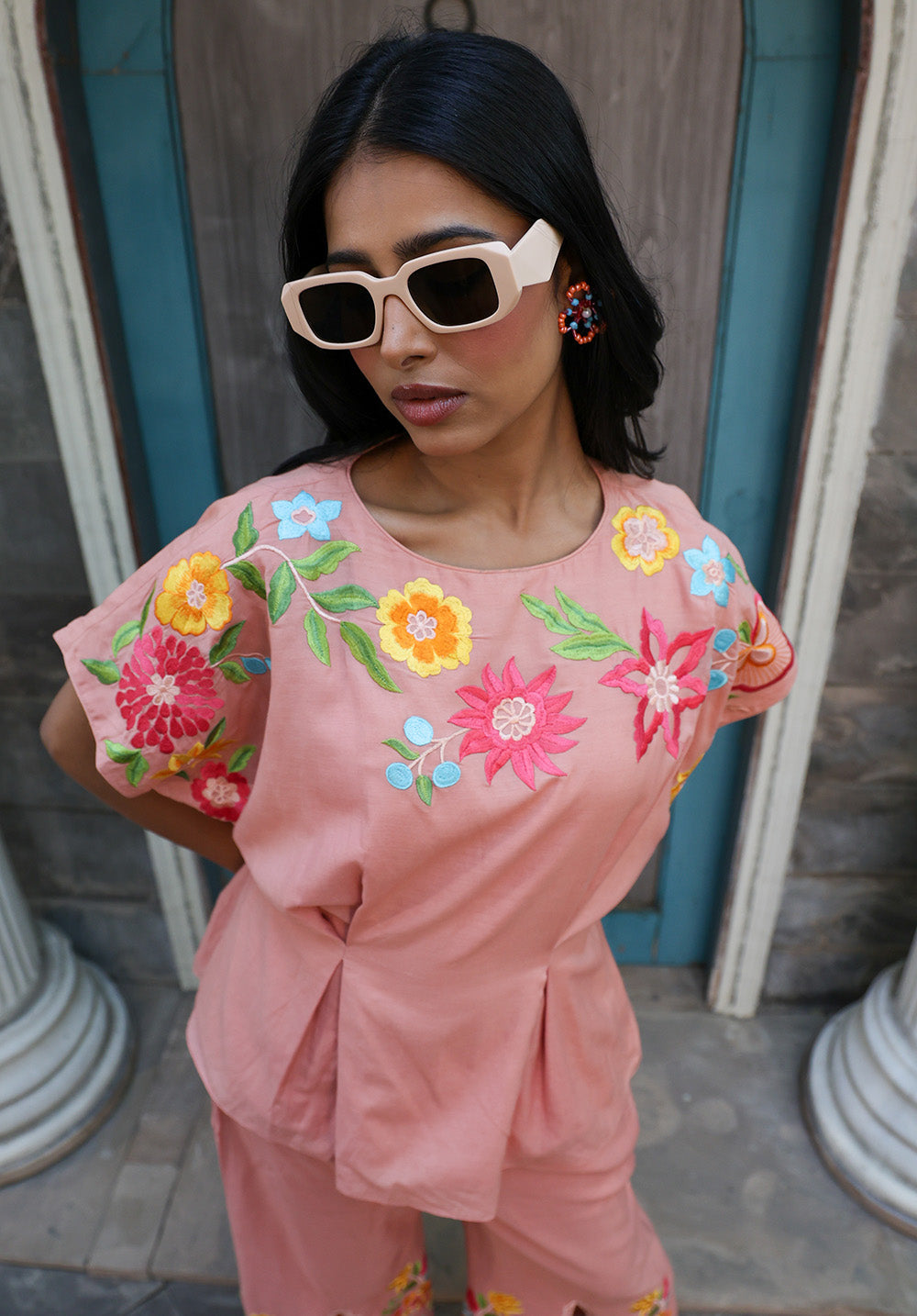 Close-up of peach embroidered top with colorful floral embroidery and pleated waist detailing