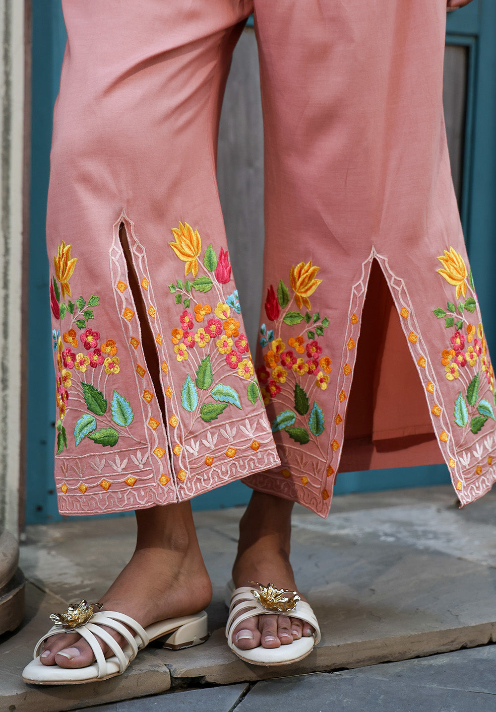 Close-up of peach pants featuring floral embroidery and slit hem detailing